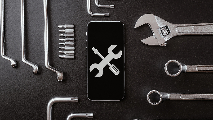 Diagnostic tools and smartphone repair concept with phone screen showing wrench and screwdriver icon surrounded by metal tools.