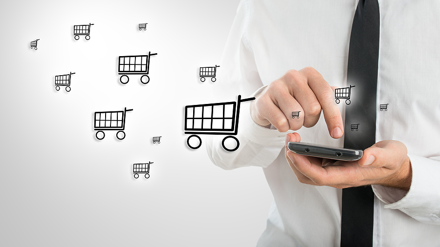 Businessman using a smartphone with shopping cart icons symbolizing mobile e-commerce and online phone purchases.