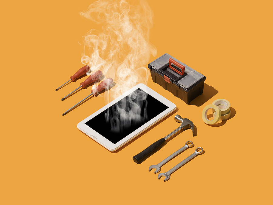 smartphone emitting smoke lies on an orange surface surrounded by repair tools, including screwdrivers, wrenches, a hammer, tape, and a small toolbox, symbolizing phone overheating and repair.