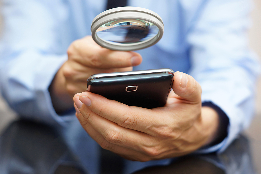 A person examining a smartphone closely using a magnifying glass, inspecting the device for authenticity or issues.