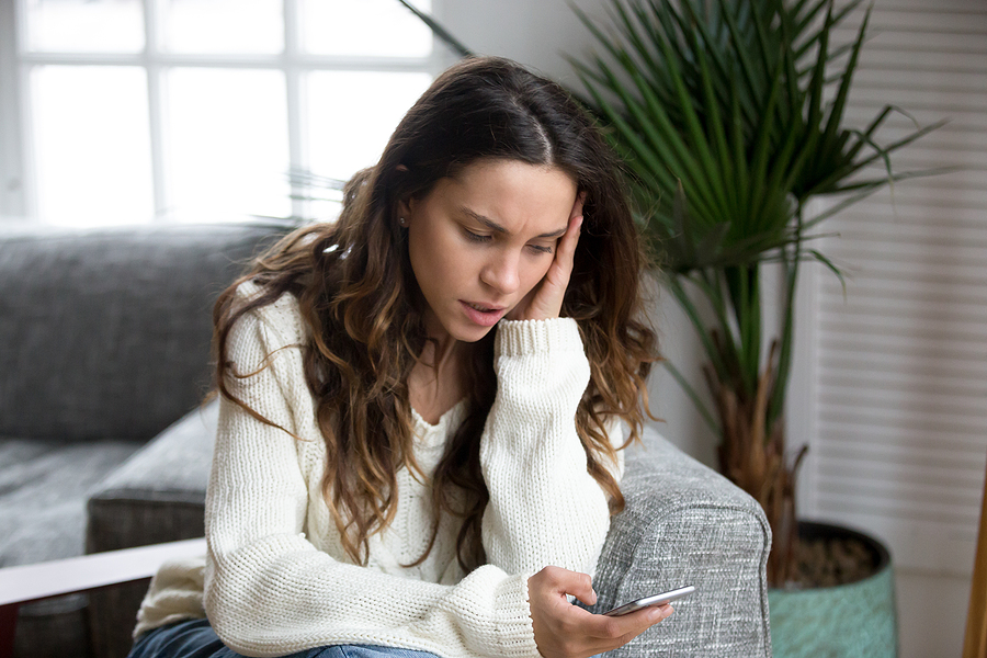 Concerned woman looking at her smartphone, representing the importance of reviewing used phone reports and understanding a device history report before buying.