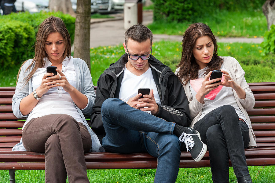 Three people sitting on park bench spending time on their mobile phones.
